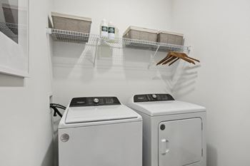 A laundry room with a washer and dryer and a shelf with baskets and a handbag